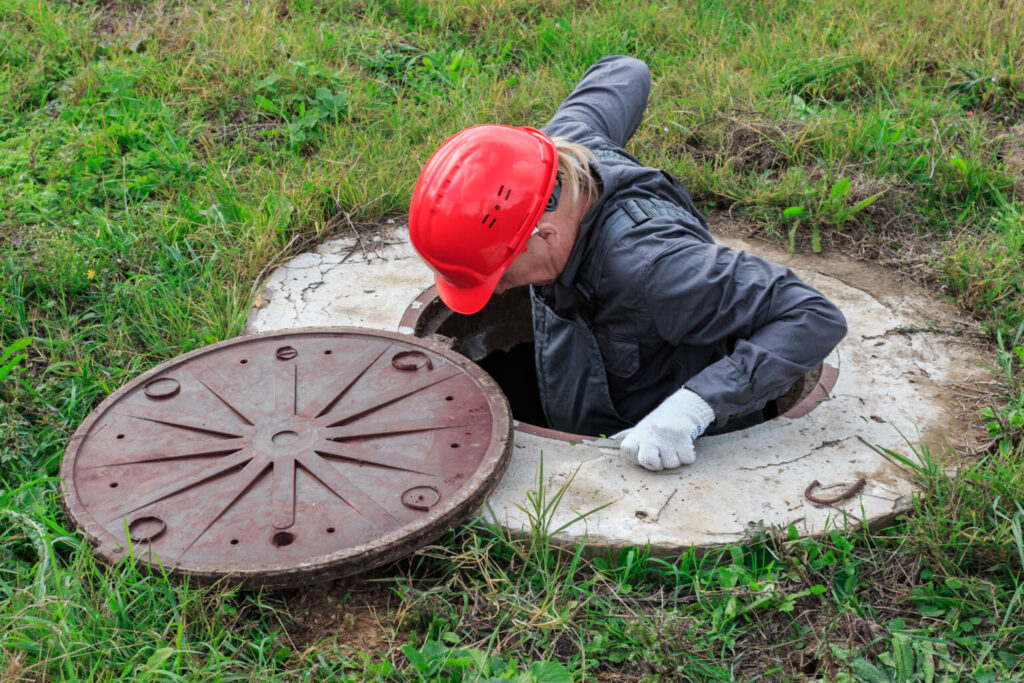 Technician in a safety helmet working inside an open access well to inspect and repair the system
