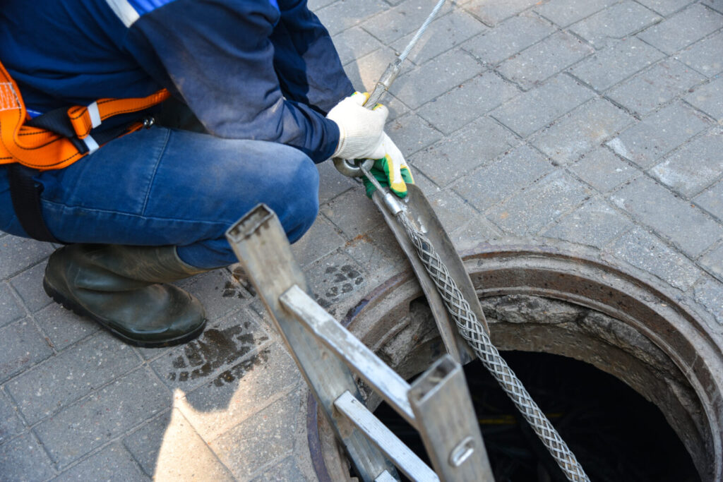 Two workers servicing underground lines inside an open well